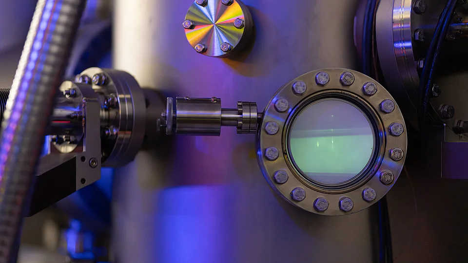 Close-up of a stainless-steel vacuum chamber viewport with a bolted flange, part of a molecular beam epitaxy (MBE) system.